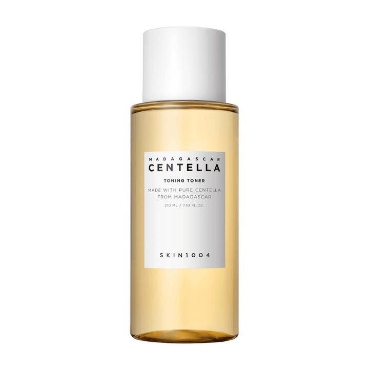 Obrázok zobrazuje fľašu s pleťovým tonerom, označenú ako "Madagascar Centella Toning Toner" od SKIN1004. Produkt je uvedený ako obsahujúci 210 ml alebo 7,10 fl.oz a je vyrobený s čistou Centellou z Madagaskaru. Balenie je jednoduché a elegantné s priehľadnou fľašou a zlatistou tekutinou vo vnútri, čo vytvára pocit luxusu a čistoty. Logo značky SKIN1004 je jasne viditeľné v dolnej časti etikety.