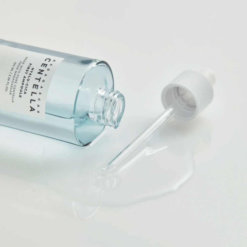 Detailný záber na otvorenú fľašu Skin1004 Madagascar Centella Hyalu-Cica First Ampoule s ležiacou pipetou a sérom rozliatym na bielom povrchu.