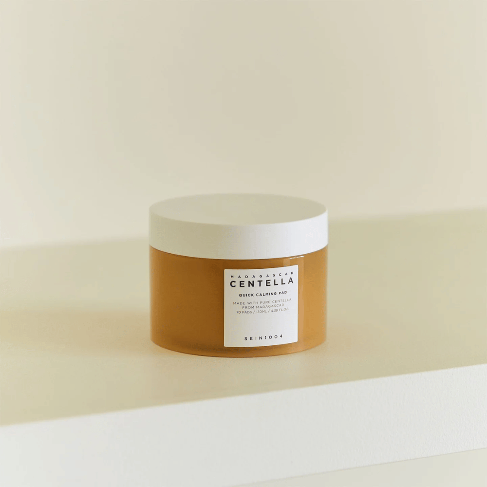 SKIN1004 Madagascar Centella Quick Calming Pad umiestnený na bielej poličke – jantárová nádoba s bielym viečkom a výraznou etiketou vpredu.
