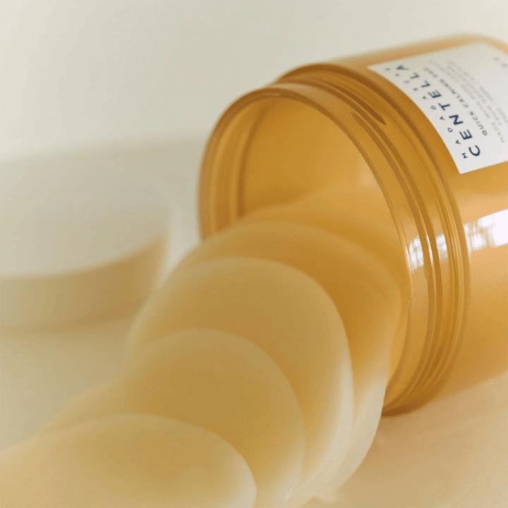 Otvorená nádoba s SKIN1004 Madagascar Centella Quick Calming Pad – niekoľko okrúhlych tonizačných podložiek v svetložltej tekutine je vidieť, nádoba je jantárová s bielou etiketou.