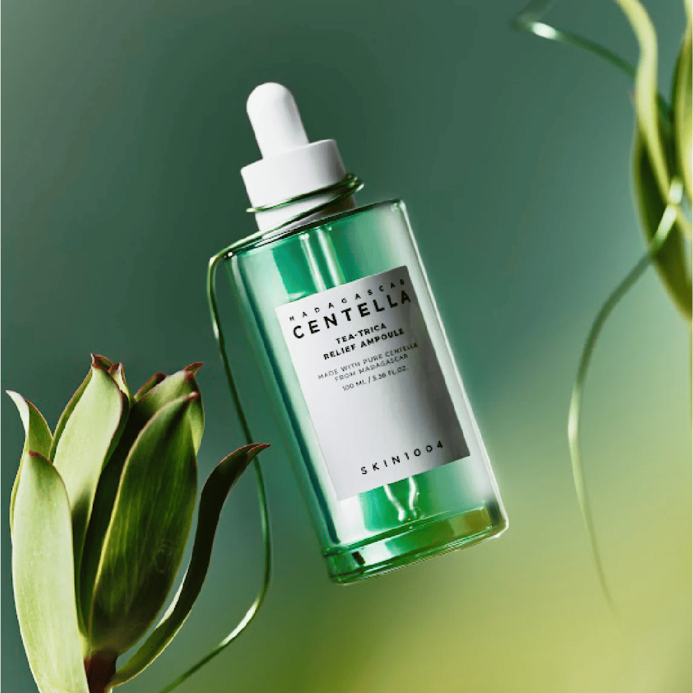 SKIN1004 Madagascar Centella Tea-Trica Relief Ampoule – zelená sklenená fľaša s pipetou, bielou etiketou a obsahom 100 ml, fotografovaná na zelenom pozadí s rastlinnými detailmi.