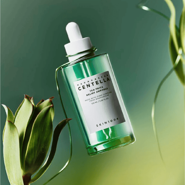 SKIN1004 Madagascar Centella Tea-Trica Relief Ampoule – zelená sklenená fľaša s pipetou, bielou etiketou a obsahom 100 ml, fotografovaná na zelenom pozadí s rastlinnými detailmi.