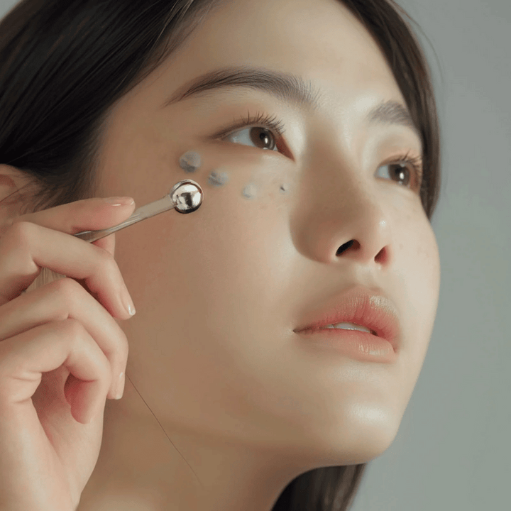 Žena aplikuje Heimish Marine Care Algae + Peptide Eye Cream pod oko s kovovým aplikátorom pre chladivý a osviežujúci efekt. Krém pomáha hydratovať a redukovať známky starnutia okolo očí.