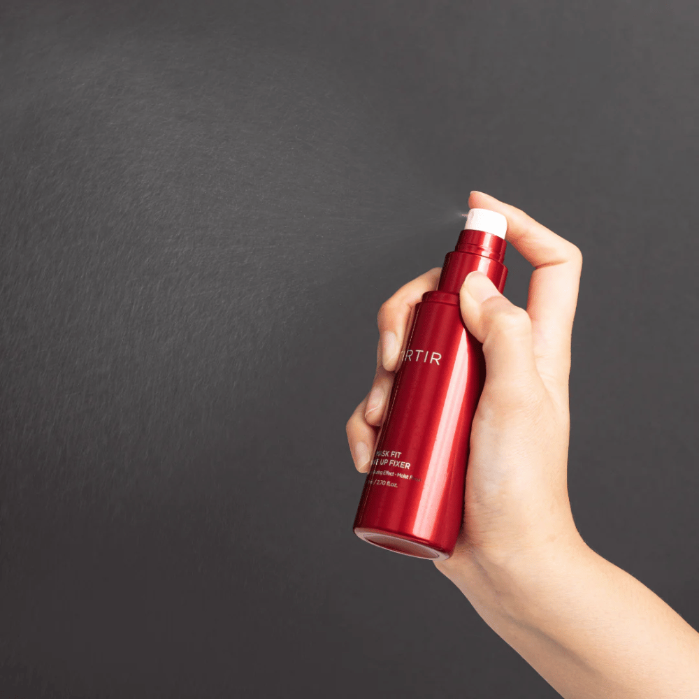 Ruka držiaca červenú fľašu značky tirtir Mask Fit Make Up Fixer a rozprašujúca jemnú hmlu, ideálnu na fixáciu make-upu.