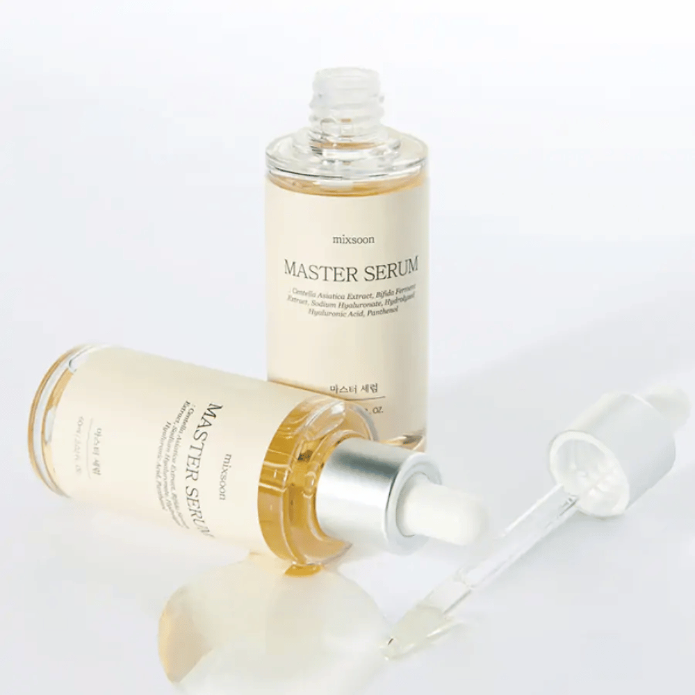 Dve fľaše Mixsoon Master Serum, jedna stojaca a druhá ležiaca s otvorenou pipetou, kde sérum vyliate na biely povrch.