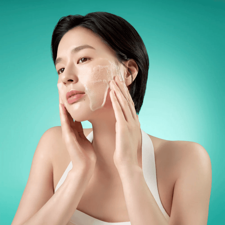 Žena čistí tvár jemnou penivou čistiacou penou na tvár na zelenom pozadí.