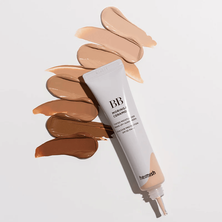 Heimish Moringa Ceramide BB Cream obklopený viacerými vzorkami odtieňov v rôznych tónoch pleti. Obrázok ukazuje širokú škálu farieb produktu a krémovú konzistenciu, ktorá poskytuje prirodzené krytie a jednotný tón pleti.