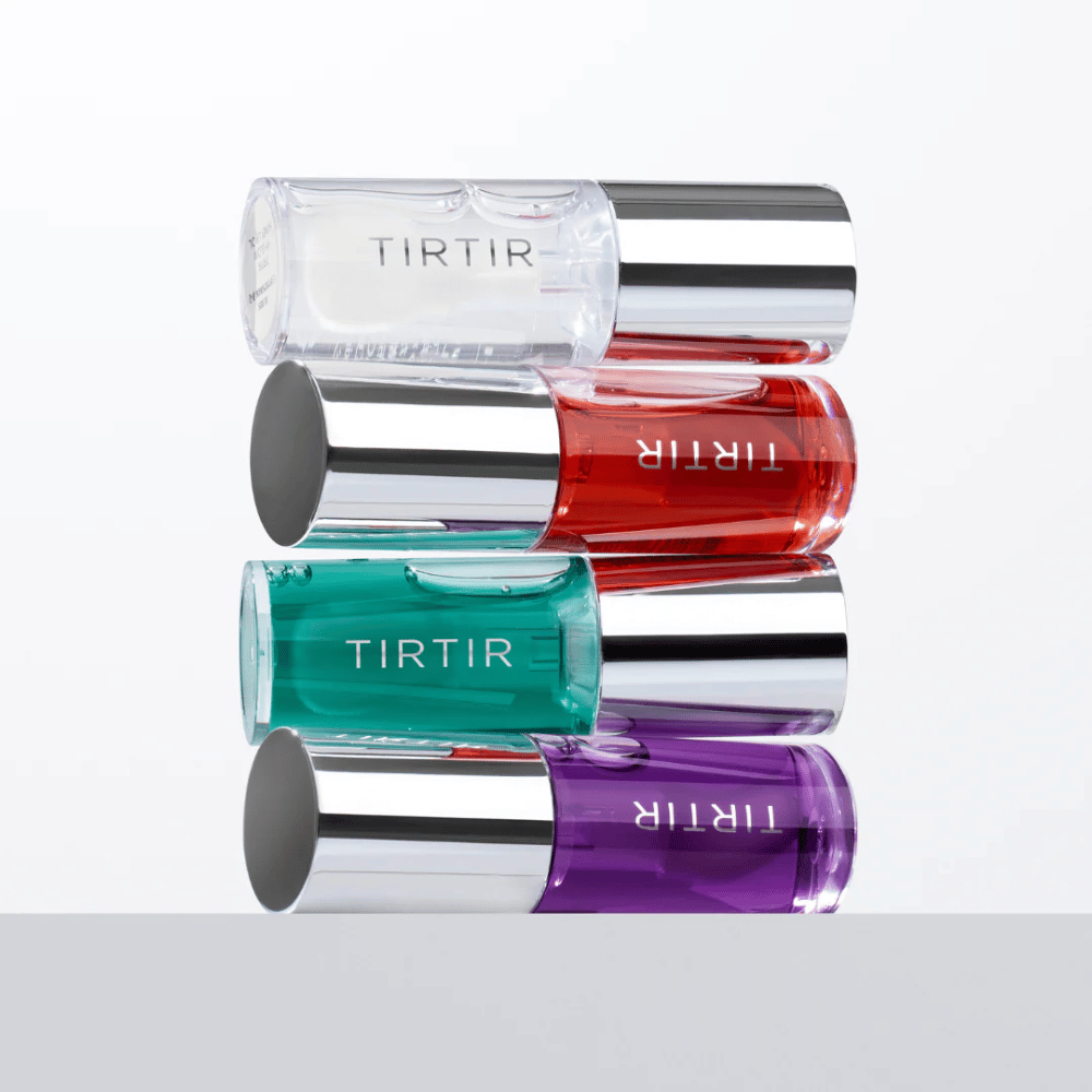 Štyri TIRTIR My Glow Lip Oil v rôznych farbách – priehľadná, červená, zelená a fialová – naskladané na sebe so striebornými uzávermi na bielom pozadí.