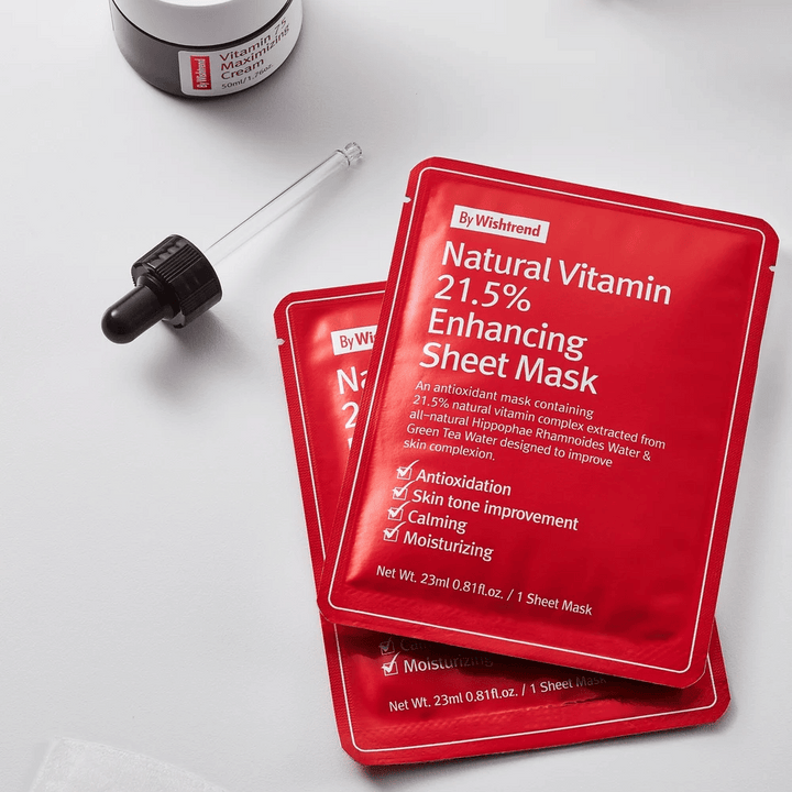 By Wishtrend Natural Vitamin 21.5% Enhancing Sheet Mask v červených baleniach, umiestnené na bielej ploche spolu s pipetou a nádobou pleťového krému.