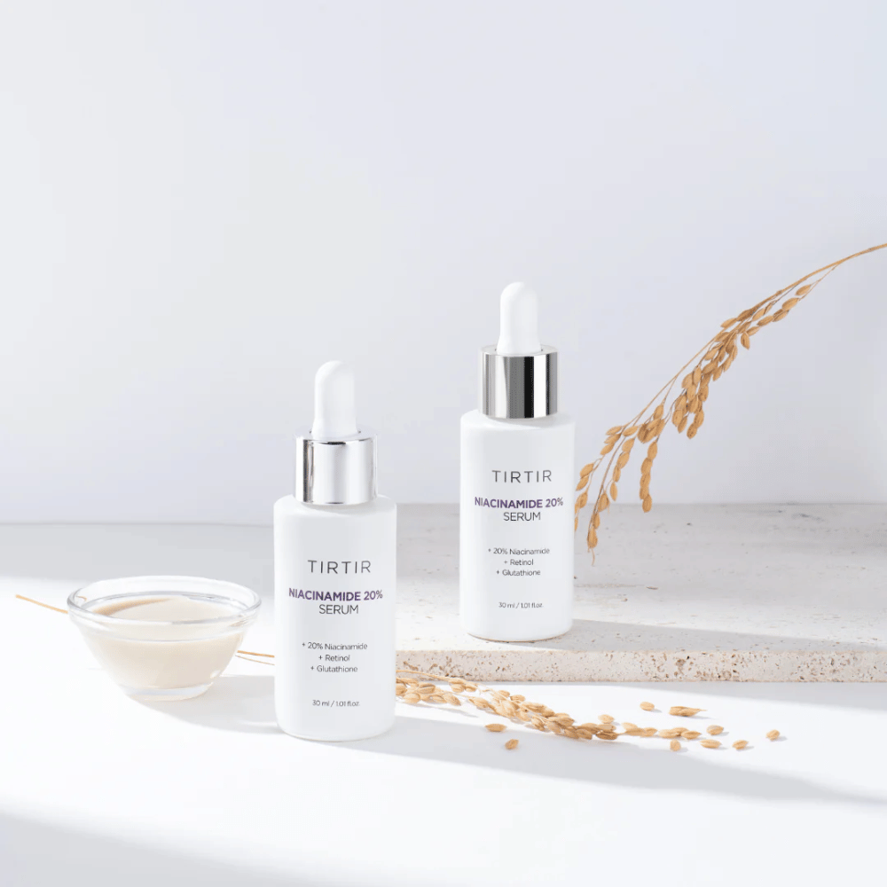 Dve fľaše Tirtirs "Niacinamide 20% Serum" sú zobrazené na svetlom povrchu spolu s malou miskou s krémovou substanciou a niekoľkými steblami suchých rastlín. Sérum obsahuje 20 % niacínamidu, retinolu a glutatiónu, čo prispieva k zlepšeniu vzhľadu a textúry pokožky.