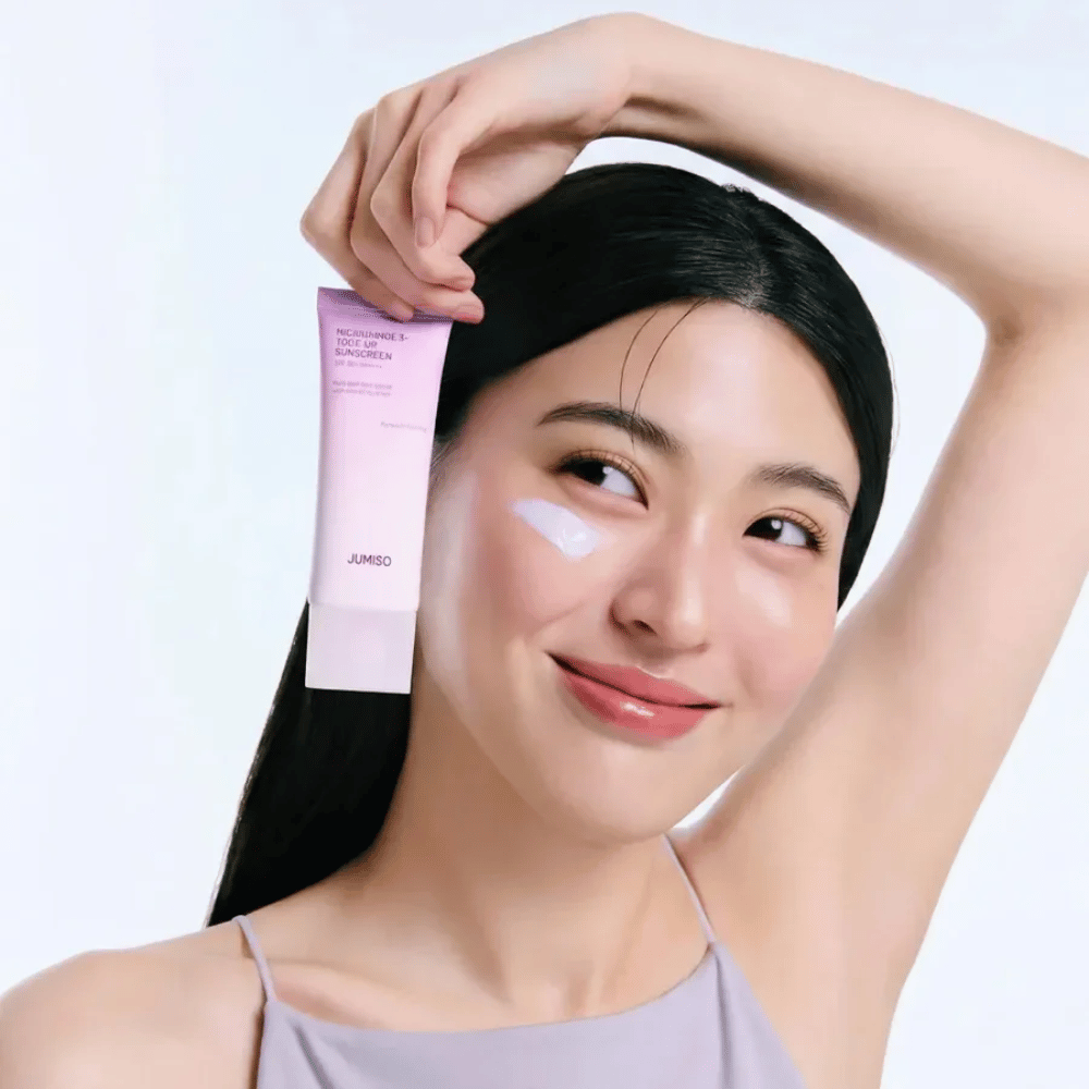 Modelka drží JUMISO Niacinamide 3+ Tone-Up Sunscreen SPF50+ PA++++ – opaľovací krém s niacínamidom, ktorý zjednocuje tón pleti a chráni pokožku.