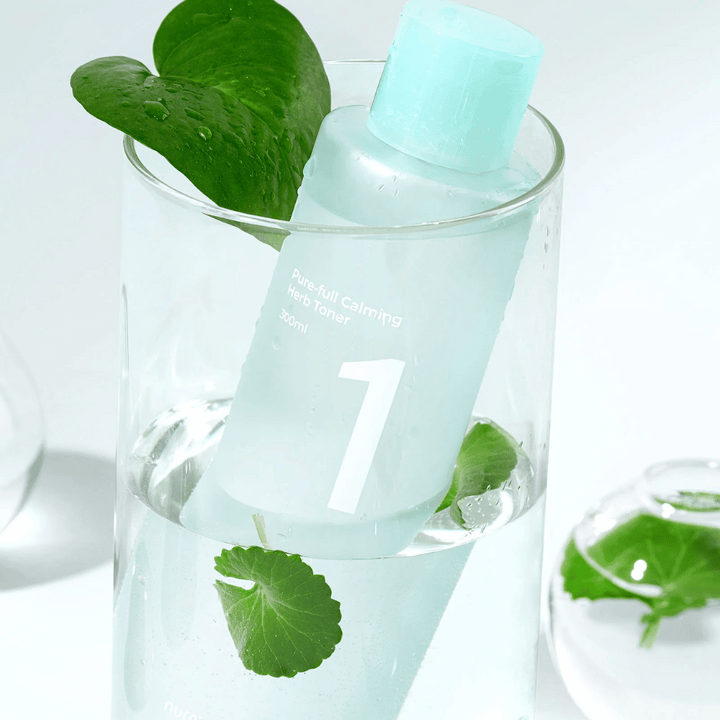 Fľaša s No.1 Pure-Full Calming Herb Toner umiestnená v pohári s vodou a zelenými listami. Fľaša má svetlomodrý uzáver a etiketu s textom "Pure-full Calming Herb Toner" a "300ml". Produkt vyzerá sviežo s vodou a vegetáciou v pozadí, čo vytvára upokojujúci a prirodzený pocit.