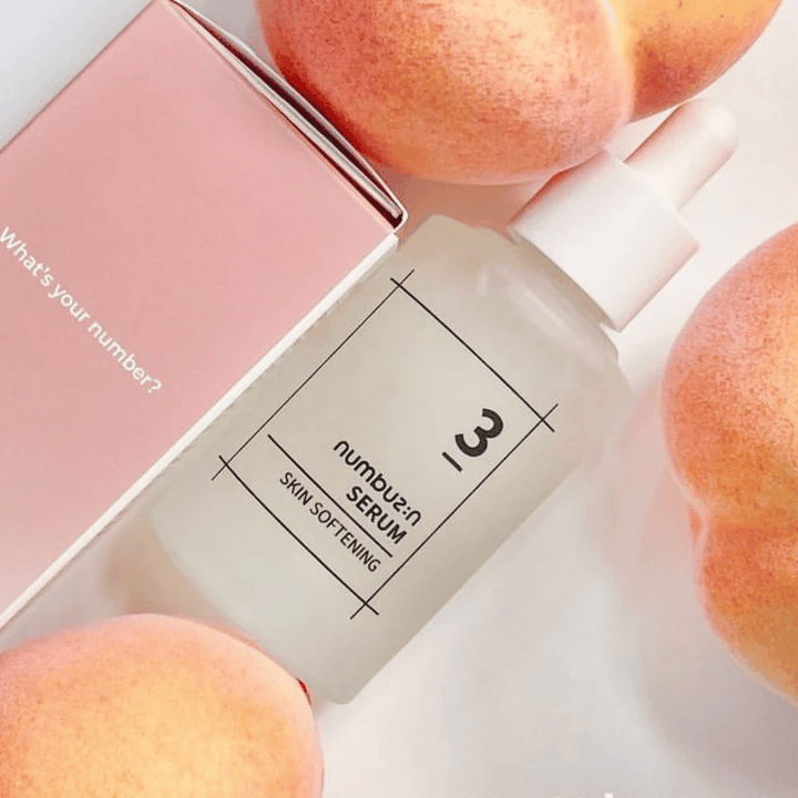 Fľaša s numbus:in No.3 sérom na zjemnenie pokožky obklopená broskyňami a ružovou škatuľou s textom "Aké je tvoje číslo?".