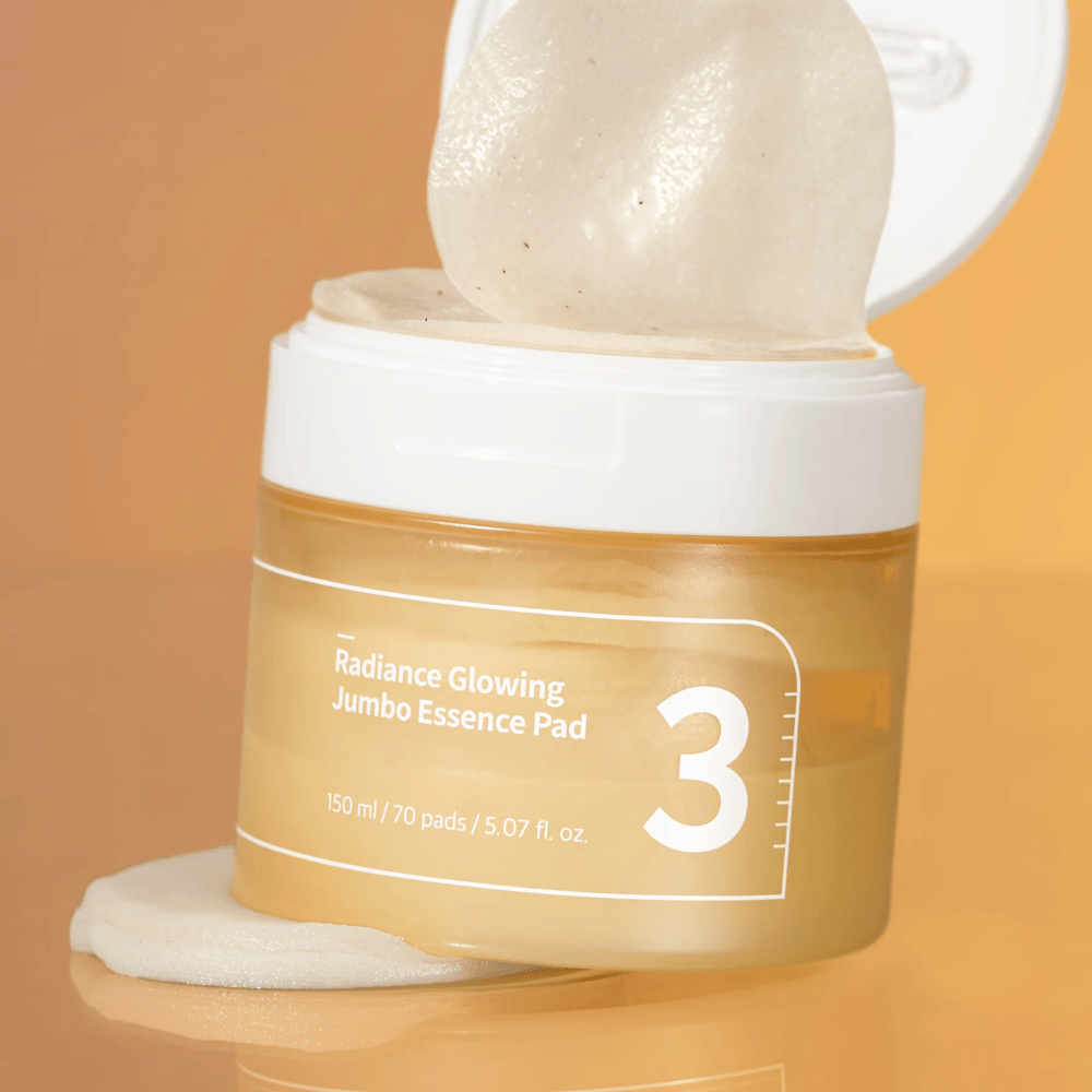 Otvorená nádoba s numbuzin No. 3 Radiance Glowing Jumbo Essence Pad, jedna podložka je opretá o okraj, pozadie v oranžovom tóne.