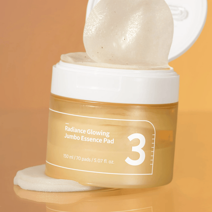 Otvorená nádoba s numbuzin No. 3 Radiance Glowing Jumbo Essence Pad, jedna podložka je opretá o okraj, pozadie v oranžovom tóne.