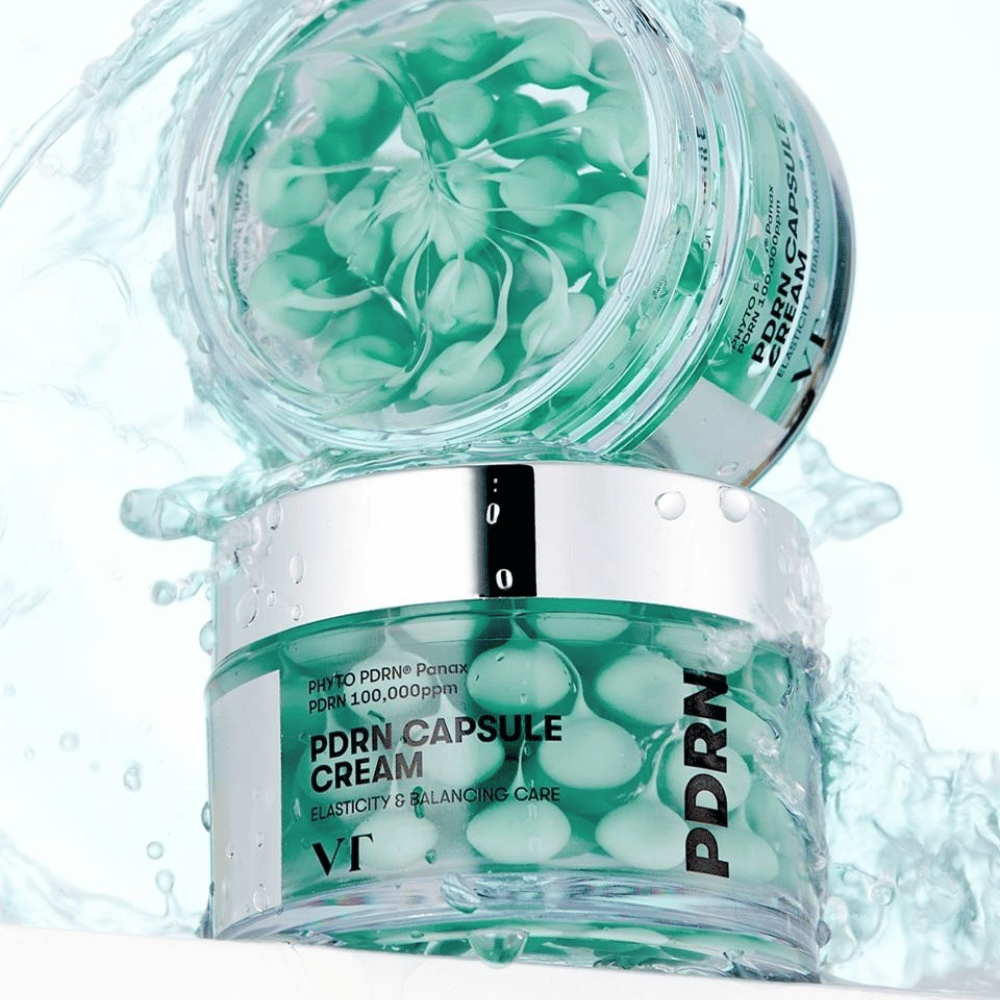 Dve nádoby VT PDRN Capsule Cream naskladané s rozstrekmi vody okolo. Priehľadné nádoby ukazujú zelené kapsuly vo vnútri, s textom "Elasticity & Balancing Care" viditeľným na etikete.
