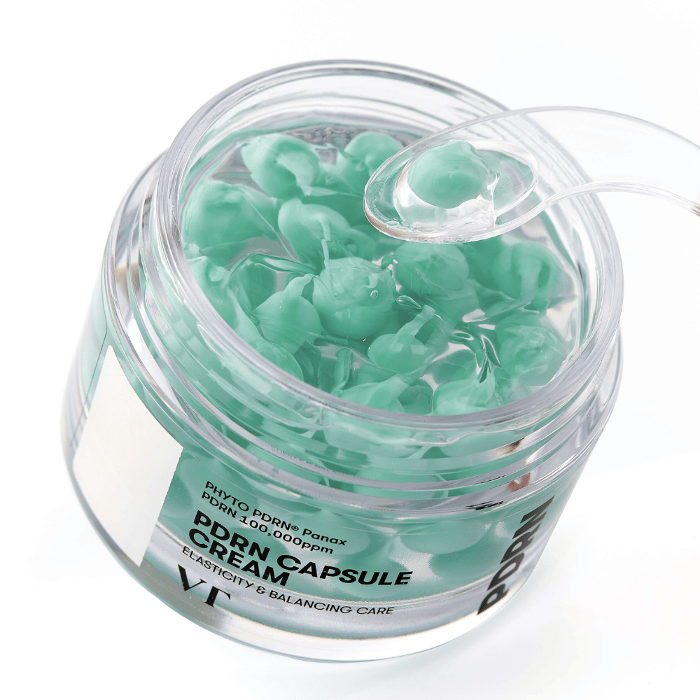 Detailný záber na otvorenú nádobu s VT PDRN Capsule Cream. Obsahuje malé zelené kapsuly v priehľadnom géli, s priloženou špachtľou na aplikáciu. Text na nádobe znie "Elasticity & Balancing Care".