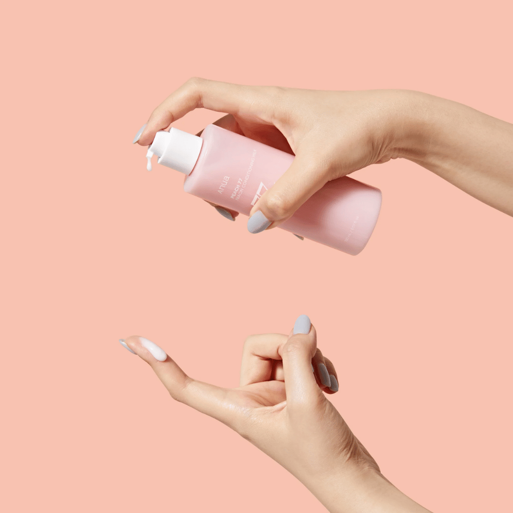 Obrázok ukazuje niekoho ruky, ktoré držia fľašu s ANUA Peach 77% Niacin Conditioning Milk. Tento produkt na starostlivosť o pleť má mliečnu konzistenciu a je navrhnutý na starostlivosť a zlepšenie stavu pokožky.