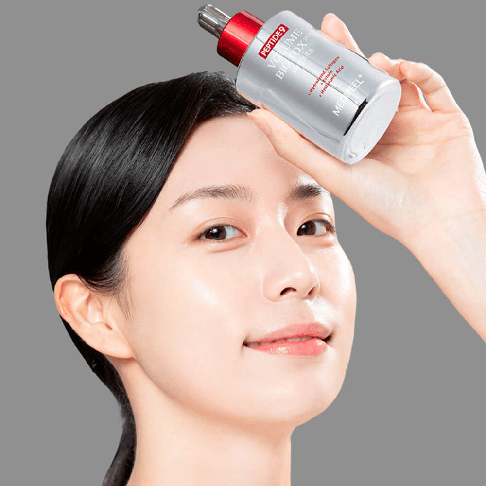 Osoba drží MEDI-PEEL Peptide 9 Volume Bio Tox Pro Ampoule pri čele. Pokožka vyzerá hydratovaná a žiarivá – sérum posilňuje elasticitu a pevnosť.