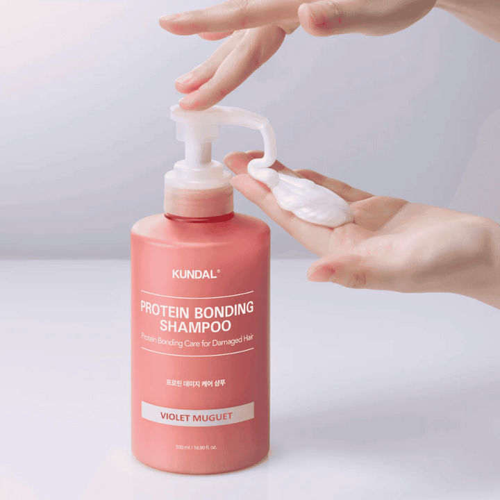 Ruka pumpuje KUNDAL Protein Bonding Shampoo Violet Muguet v krémovej konzistencii, opravný šampón pre poškodené vlasy.
