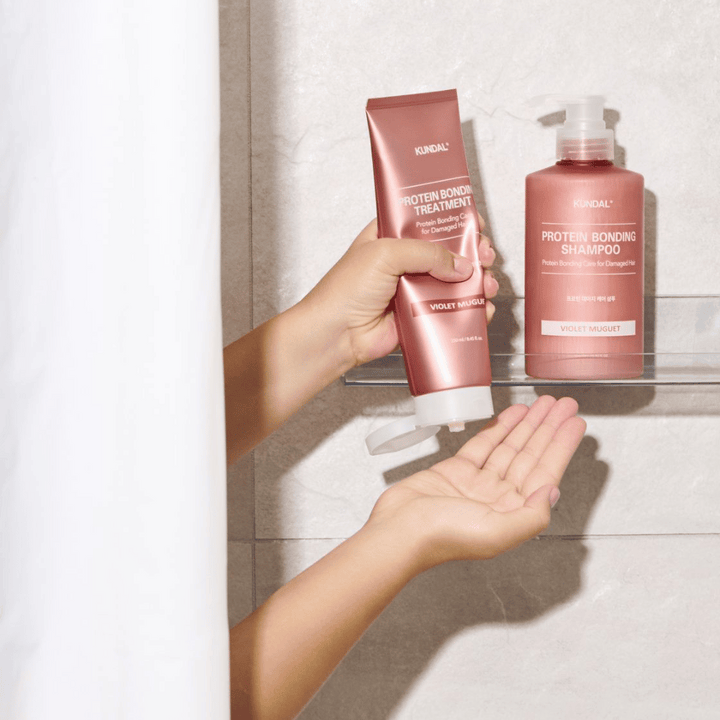 KUNDAL Protein Bonding Treatment Violet Muguet sa používa v sprche, s Protein Bonding Shampoo umiestneným na poličke vedľa.