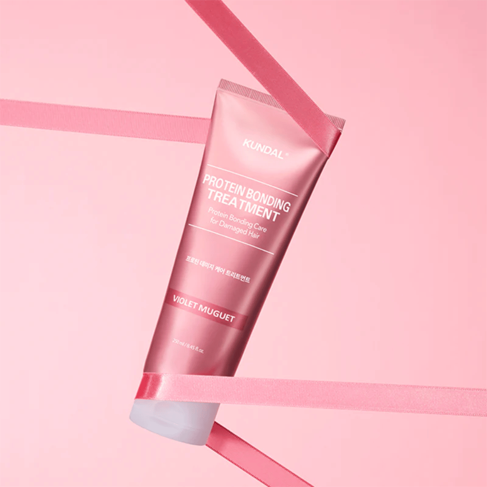 KUNDAL Protein Bonding Treatment Violet Muguet v ružovej tube 250 ml na ružovom pozadí s dekoratívnymi stuhami.