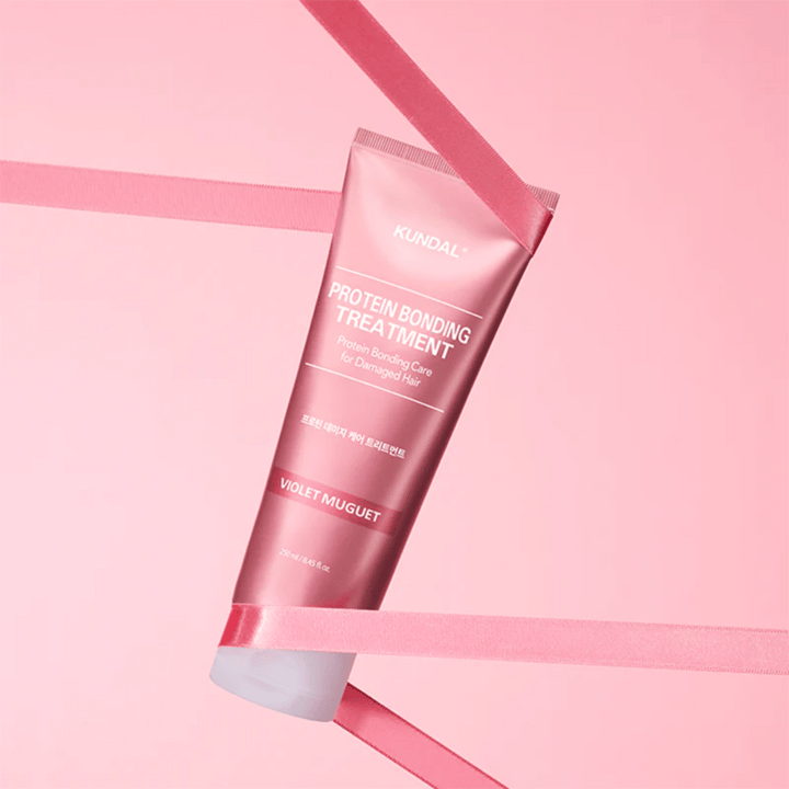 KUNDAL Protein Bonding Treatment Violet Muguet v ružovej tube 250 ml na ružovom pozadí s dekoratívnymi stuhami.