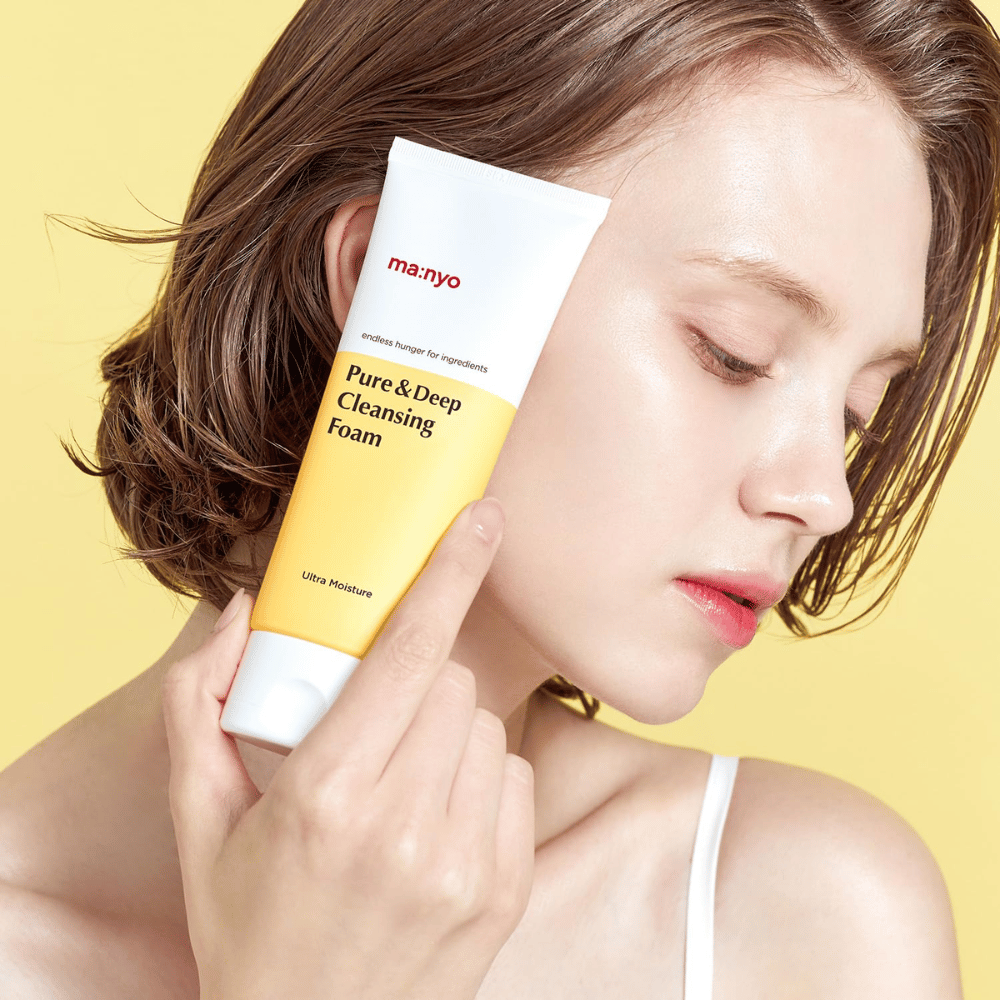 Žena so zdravou, hydratovanou pokožkou drží Ma:nyo Pure & Deep Cleansing Foam – jemné čistenie tváre, ktoré dodáva žiarivosť a rovnováhu s prírodnými ingredienciami.
