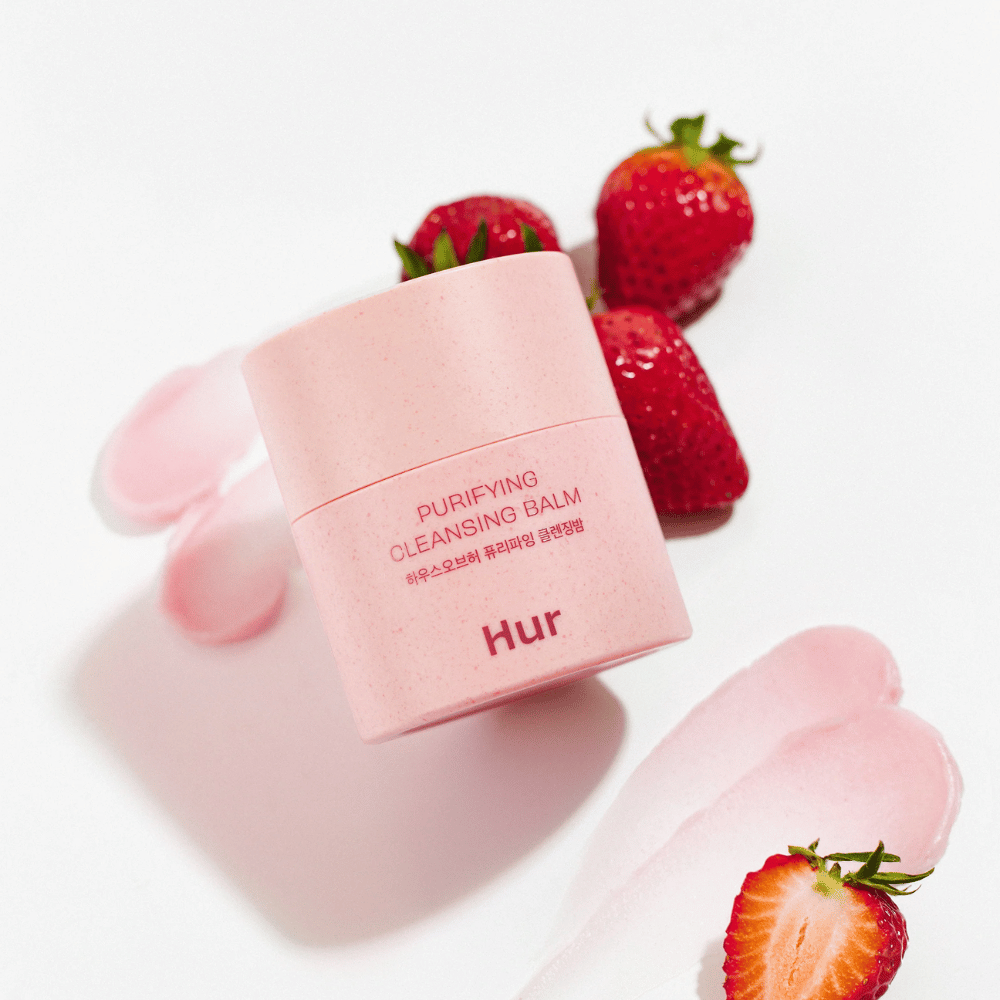 Ako Purifying Cleansing Balm umiestnený s čerstvými jahodami. Čistiaci balzam, ktorý poskytuje jemnú pokožku a je vhodný na každodenné čistenie tváre.