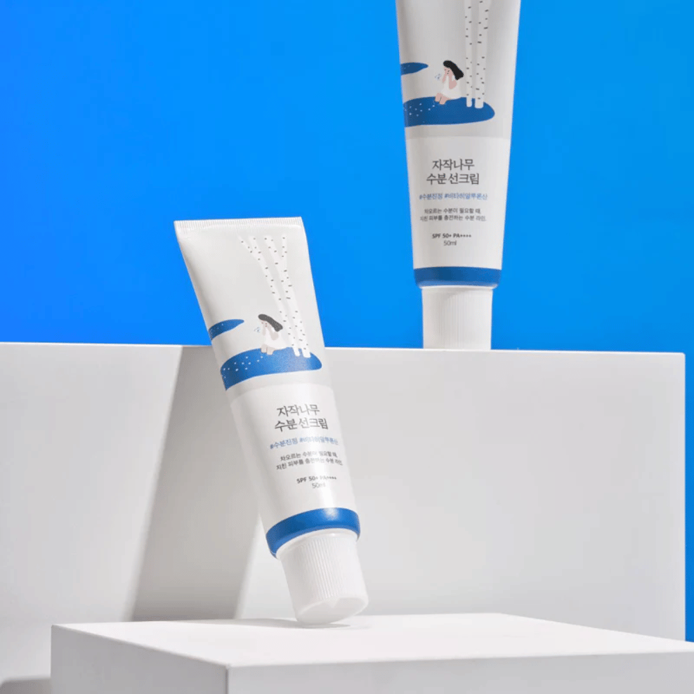 Dve tuby s Round Lab Birch Juice Moisturizing Sunscreen SPF50+ PA++++ 50ml, ktoré sú položené na modrom pozadí.