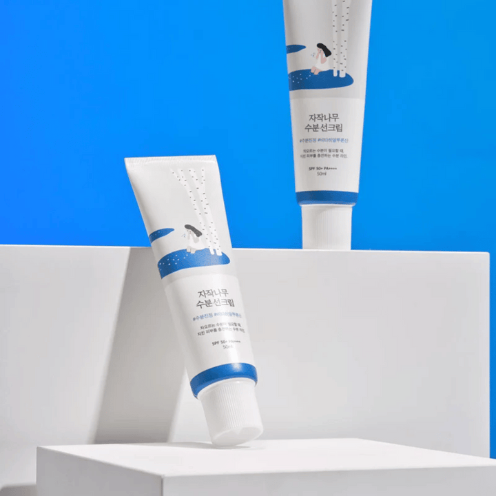 Dve tuby s Round Lab Birch Juice Moisturizing Sunscreen SPF50+ PA++++ 50ml, ktoré sú položené na modrom pozadí.