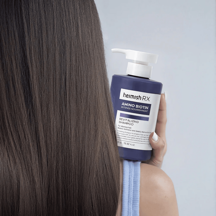 Heimish RX Amino Biotin Revitalizing Shampoo držaný v ruke pri dlhých, lesklých vlasoch – ukazuje výsledok intenzívnej výživy a hydratácie pre suché vlasy.