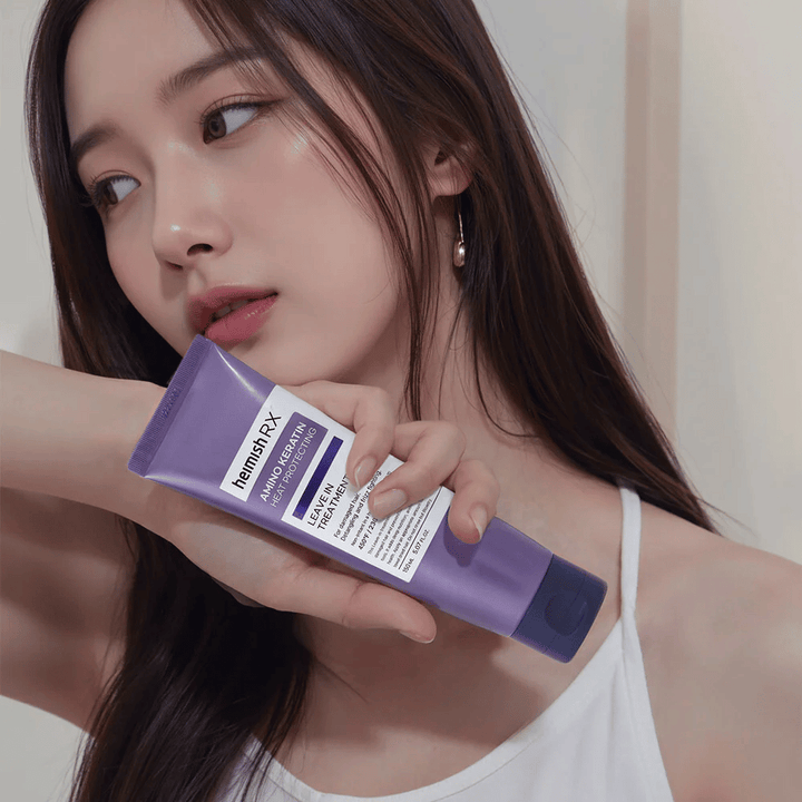 Žena s dlhými, lesklými vlasmi drží Heimish RX Amino Keratin Leave-In Treatment – ukazuje produkt ako ošetrujúci a tepelne ochranný krok v starostlivosti o vlasy.