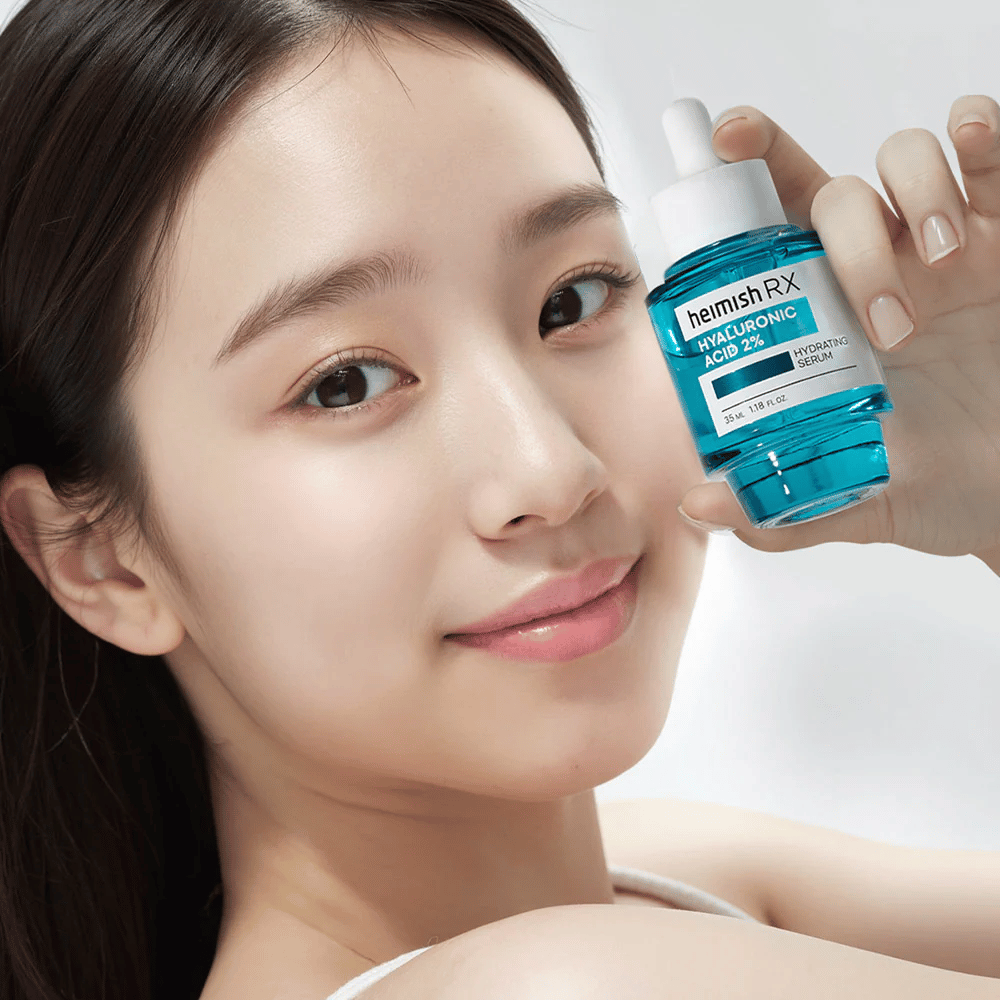 Usmievavá žena so žiarivou pokožkou drží fľašu Heimish RX Hyaluronic Acid 2% Hydrating Serum, čo zvýrazňuje jeho hydratačné vlastnosti.