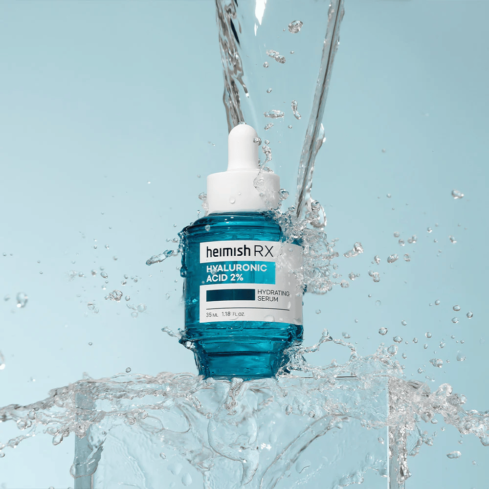 Heimish RX Hyaluronic Acid 2% Hydrating Serum umiestnené na povrchu pripomínajúcom ľad s vodou striekajúcou okolo, čo symbolizuje intenzívnu hydratáciu a sviežosť.
