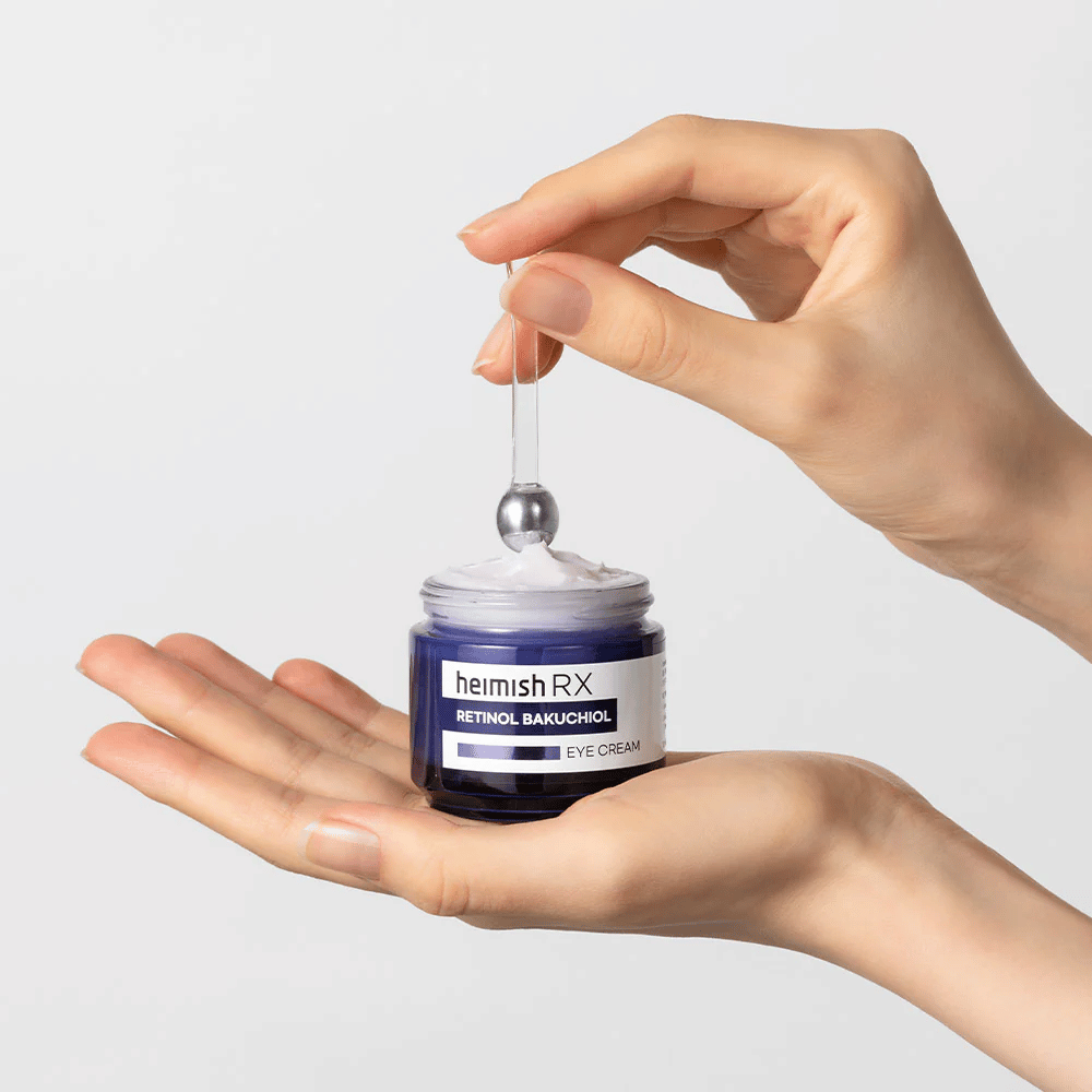 Heimish RX Retinol Bakuchiol Eye Cream v elegantnej modrej nádobe, zdvihnutý kovovým aplikátorom. Očný krém s retinolom a bakuchiolom na redukciu jemných liniek a spevnenie pokožky.