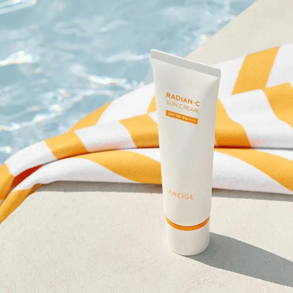 LANEIGE Radian-C Sun Cream stojí pri okraji bazéna s žlto-bielym pruhovaným uterákom v pozadí.