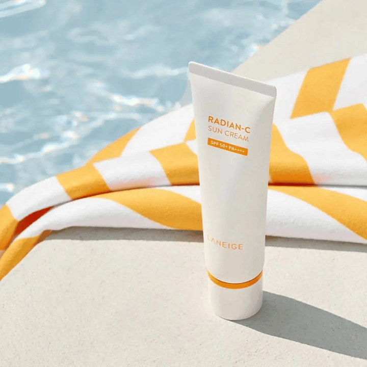 LANEIGE Radian-C Sun Cream stojí pri okraji bazéna s žlto-bielym pruhovaným uterákom v pozadí.