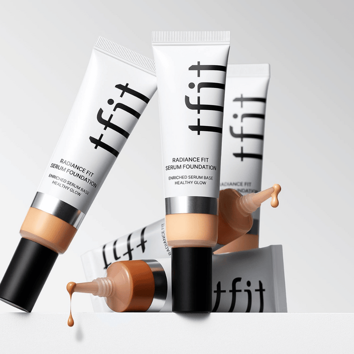 Viacero tub TFIT Radiance Fit Serum Foundation v rôznych odtieňoch, z ktorých jedna má foundation, ktorá kvapká, na svetlosivom pozadí.