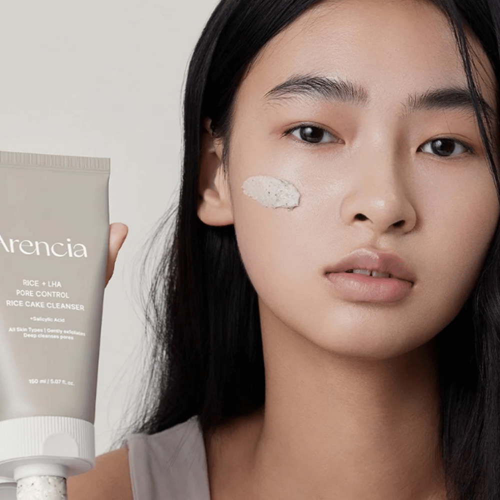 Model držiaci Arencia Rice + LHA Pore Control Rice Cake Cleanser s aplikovaným produktom na líce, ilustruje jemné, ale efektívne čistenie pórov pre denné použitie.