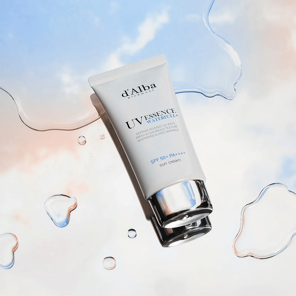 Produktový obrázok d'Alba UV Essence Waterfull+ Sun Cream so SPF 50+ PA++++, umiestnený na pozadí s vodnými kvapkami a modroružovou oblohou – symbolizuje ľahkú a hydratačnú ochranu proti slnečnému žiareniu.