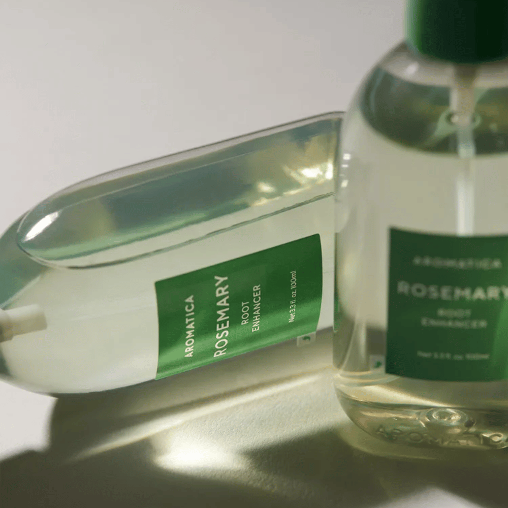 Dve fľaše AROMATICA Rosemary Root Enhancer s transparentným ochranným krytom a zelenou etiketou. Detailný záber, ktorý zvýrazňuje prémiový dizajn produktu a koncept prírodnej starostlivosti o vlasy.