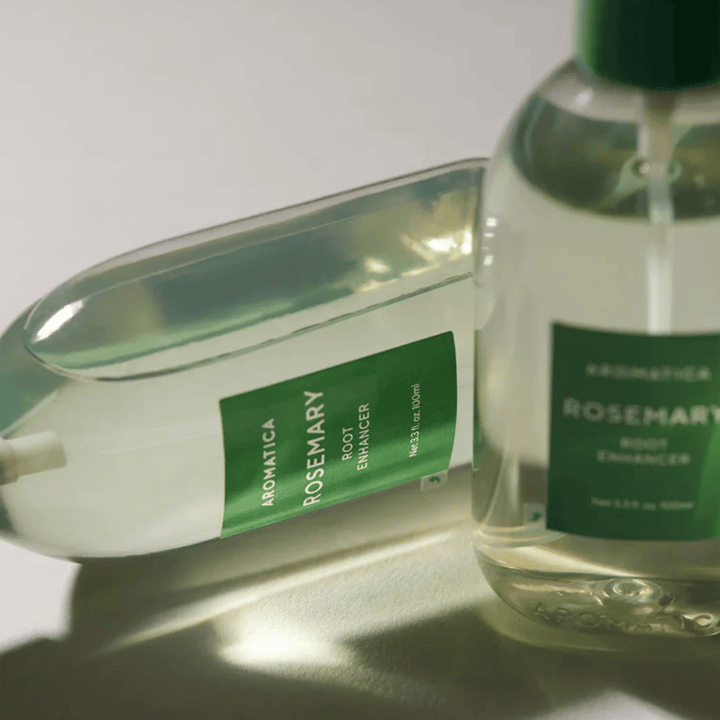 Dve fľaše AROMATICA Rosemary Root Enhancer s transparentným ochranným krytom a zelenou etiketou. Detailný záber, ktorý zvýrazňuje prémiový dizajn produktu a koncept prírodnej starostlivosti o vlasy.