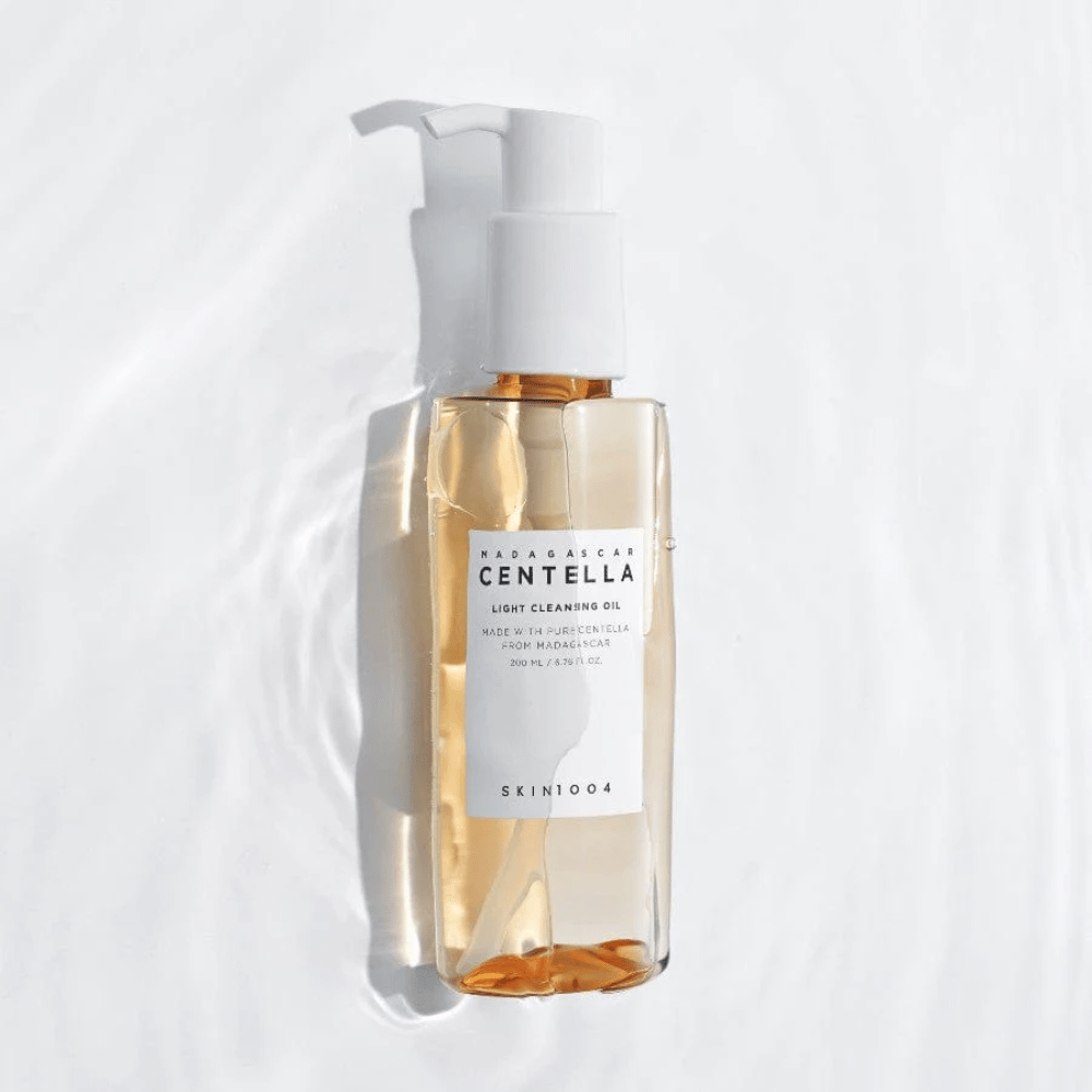 SKIN1004 Madagascar Centella Light Cleansing Oil na bielom pozadí s jemnými vodnými odrazmi, ktoré zdôrazňujú priehľadnú fľašu a zlatý obsah.