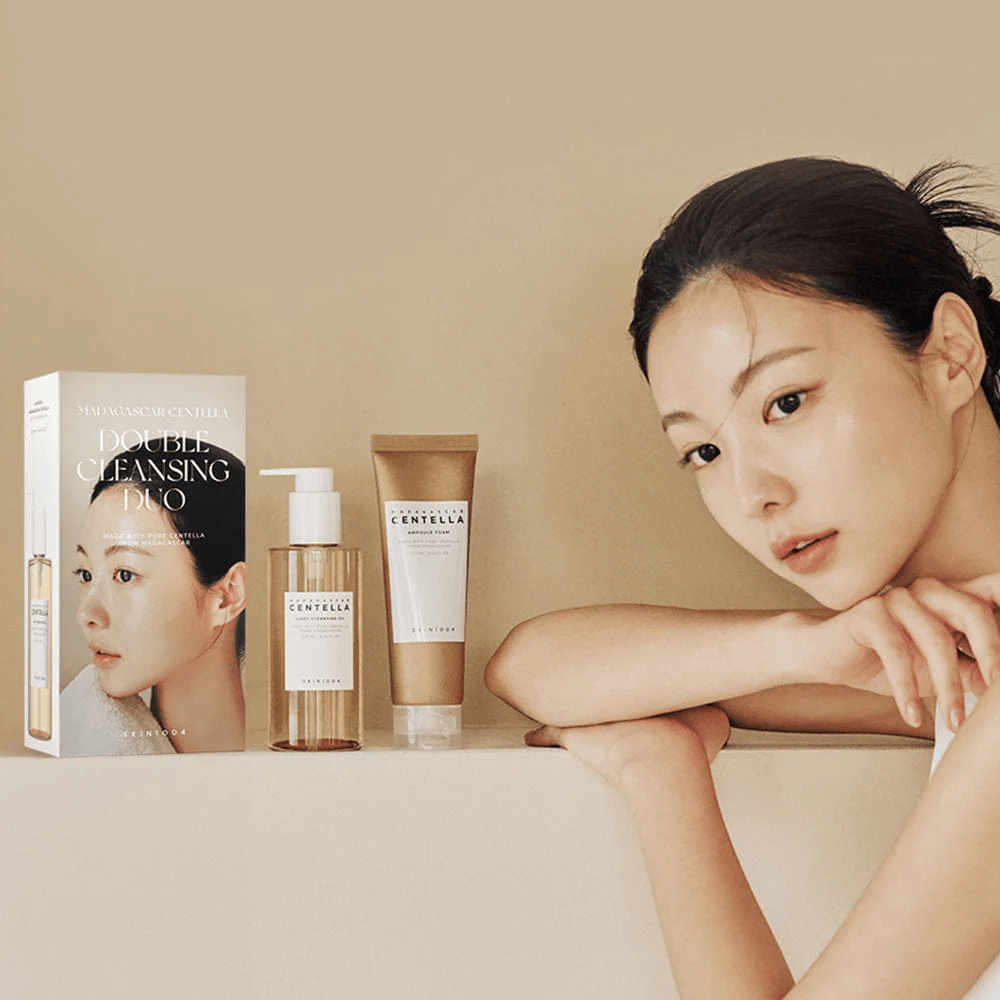 SKIN1004 Madagascar Centella Double Cleansing Duo Set s kartónom, olejovým čistením, penovým čistením a modelkou s hydratovanou pokožkou proti béžovému pozadiu.