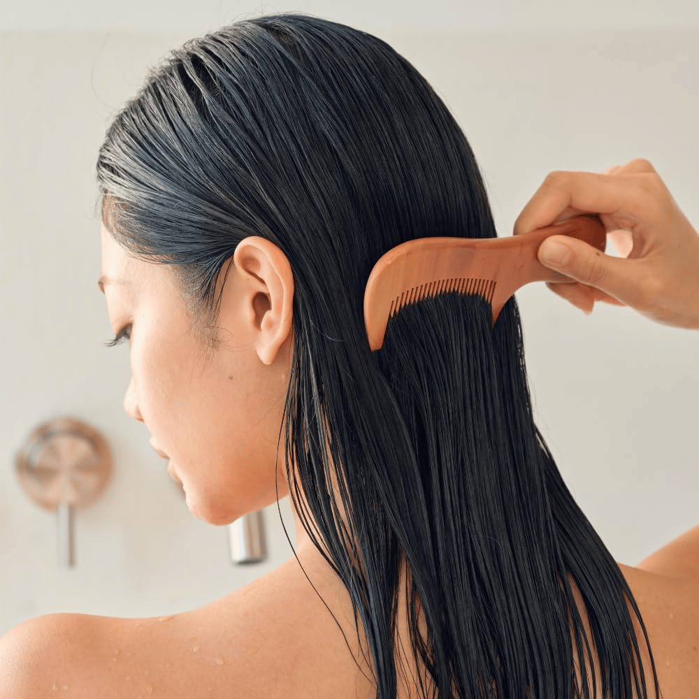 Osoba prečesáva dlhé, mokré vlasy širokým hrebeňom po aplikácii Heveblue Salmon Pullkeratin Centella Hair Treatment. Ilustruje rozčesávajúci a zjemňujúci účinok pre hladší výsledok.