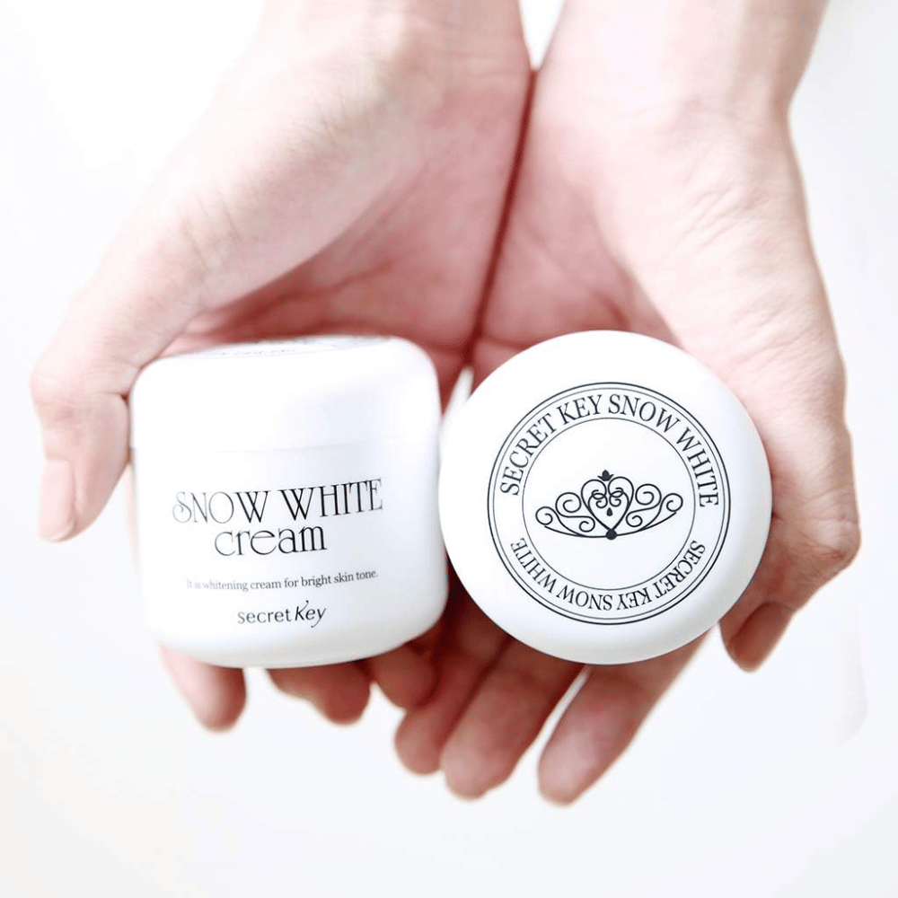 Dve nádoby Secret Key Snow White Cream držané v rukách, jedna ukazuje vrchnák a druhá prednú stranu.