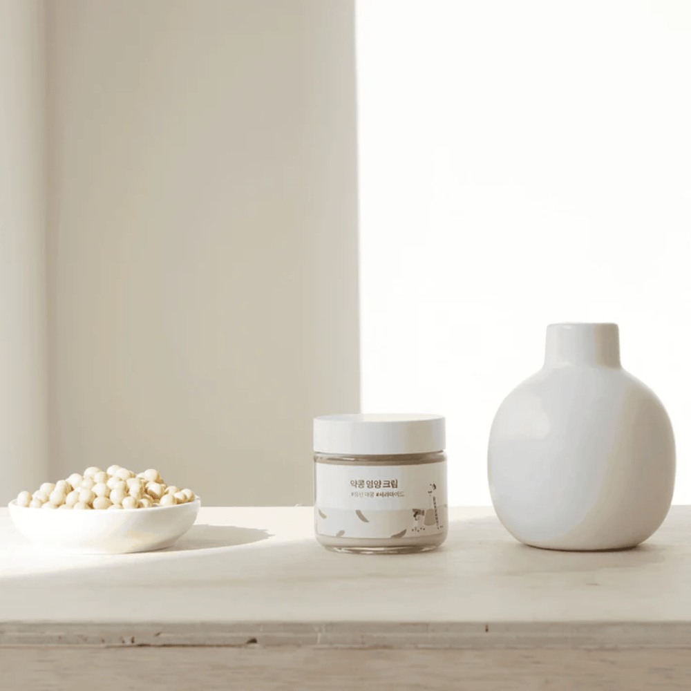 Mixsoon Soybean Nourishing Cream stojí na drevenom stole vedľa vázy a sójových bôbov. Minimalistický, hydratačný krém s prírodnými zložkami.