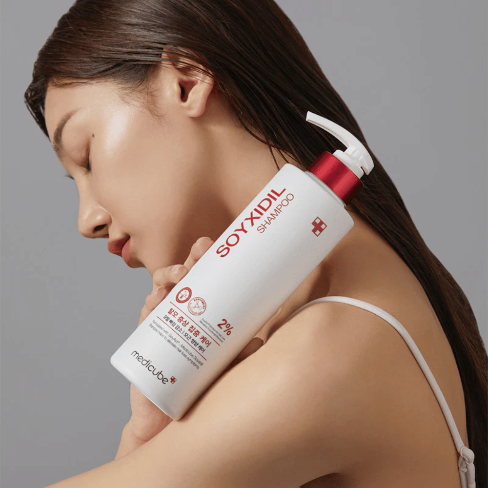 Žena s dlhými vlasmi nakláňa hlavu k fľaši Medicube Soyxidil Shampoo, ktorá posilňuje pokožku hlavy a zabraňuje vypadávaniu vlasov.