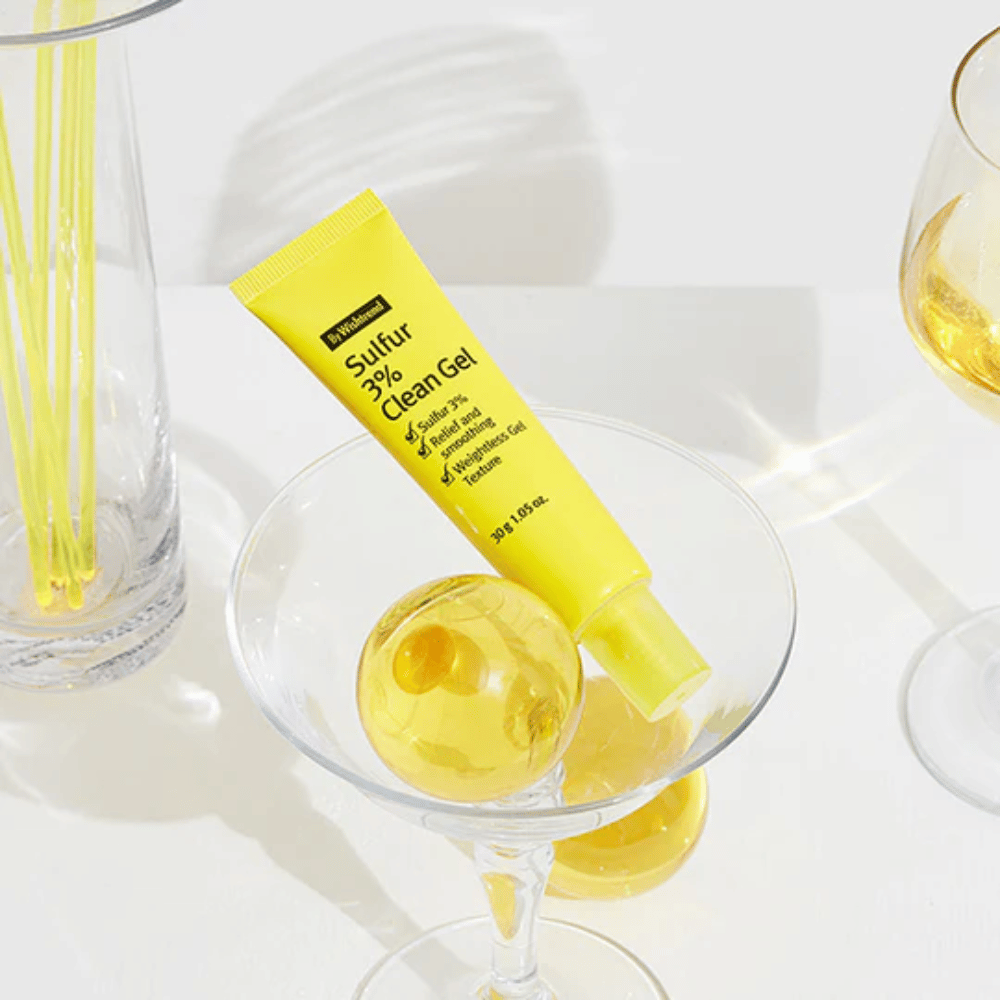 By Wishtrend Sulfur 3% Clean Gel v žltej tube umiestnený v koktailovom pohári so žltou sférou, obklopený elegantnými pohármi na bielom pozadí.